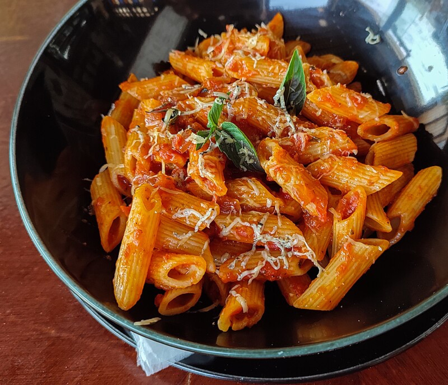 A bowl of Pastaphony Penne Arrabbiata with fresh basil and grated parmesan